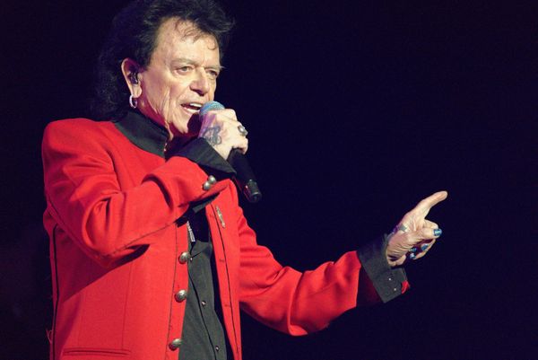 A man in a red jacket singing into a microphone on stage.