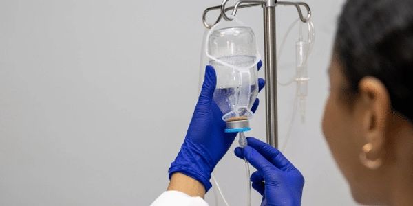 Healthcare worker adjusts IV drip wearing blue gloves.