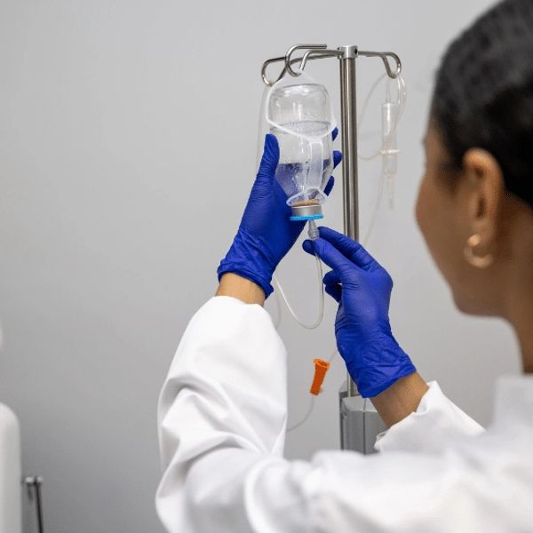 Healthcare worker adjusts IV drip wearing blue gloves.