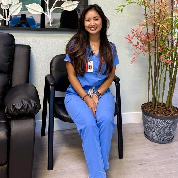 Woman in blue scrubs sitting and smiling indoors.