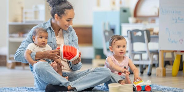 Woman playing with two babies on the floor in a bright room.