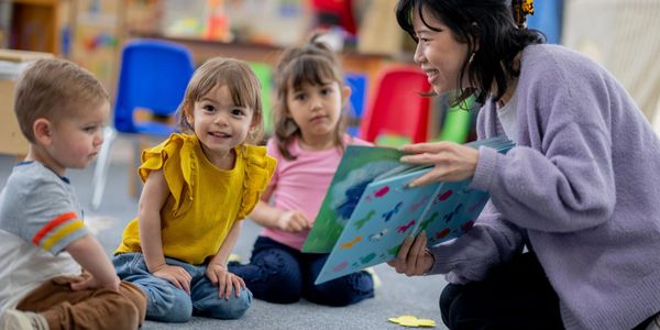 Teacher reading a book to young children in a colorful classroom.