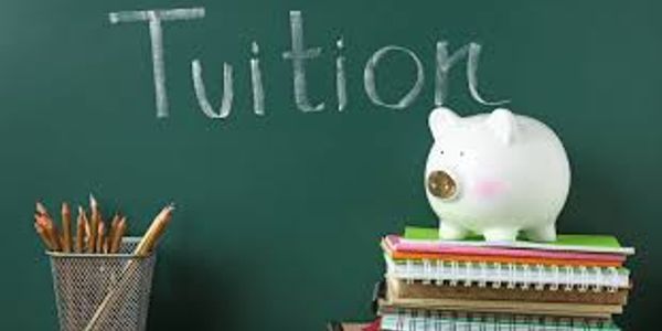 Piggy bank on books with 'Tuition' written on chalkboard.