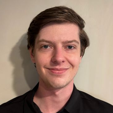 Young man with a slight smile against a beige background.
