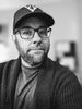 Black and white portrait of a man wearing glasses and a cap.
