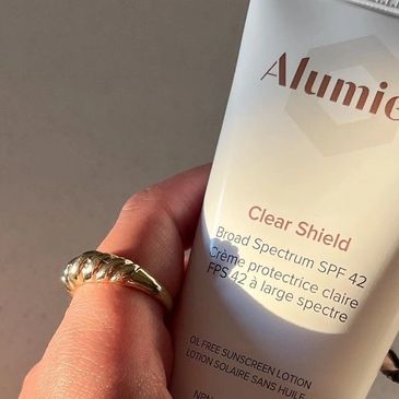 Hand holding Alumier Clear Shield SPF 42 sunscreen lotion.
