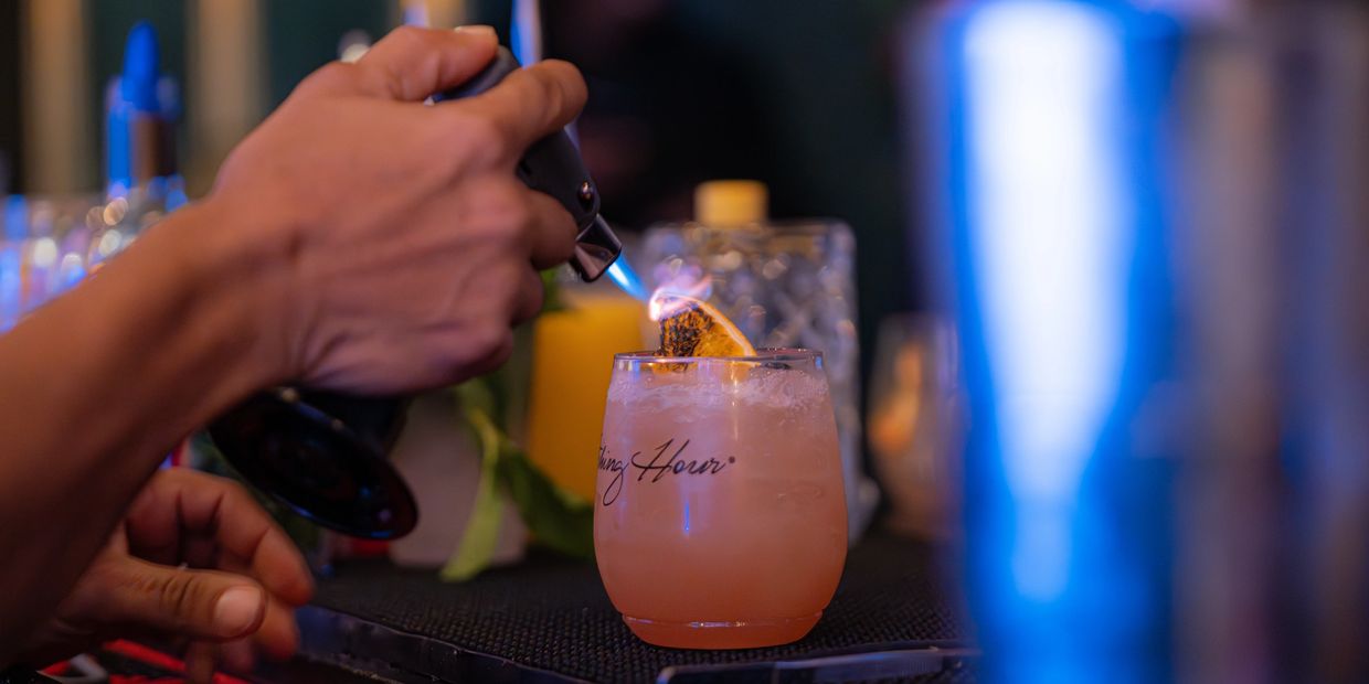 A bartender torches a citrus garnish on a cocktail glass.