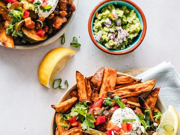 Plates of loaded sweet potato fries with guacamole and lemon wedges.