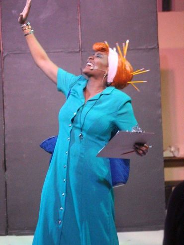 Iyana Colby dressed in a red beehive wig with pencils stuck throughout and teal dress.