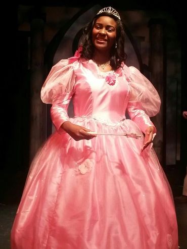 A young Iyana Colby smiling at the camera dressed in a large pink ballgown and a tiara