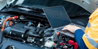 Mechanic using a laptop to diagnose a car engine problem.