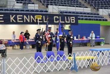 Color guard presenting flags at a kennel club event indoors.