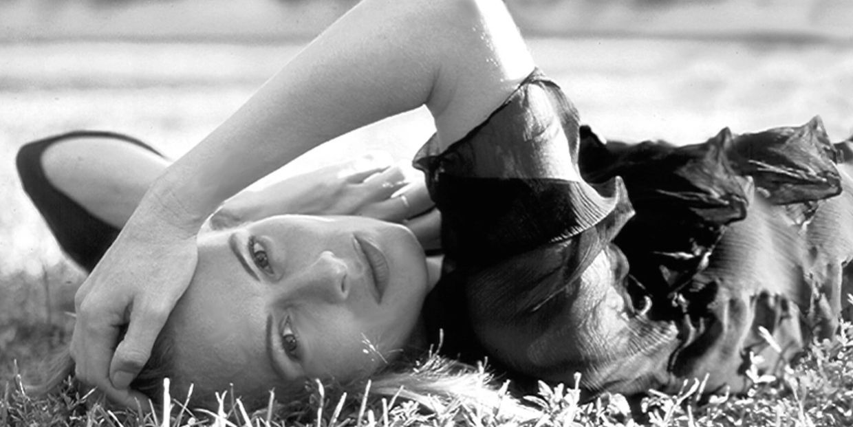 Woman lying on grass with arm over forehead in black and white.
