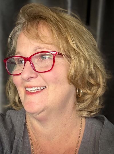 Smiling woman with blonde hair and red glasses looking to the side.