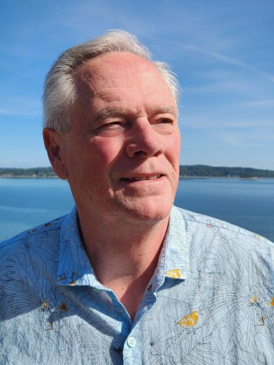 Older man in a blue patterned shirt enjoying a sunny day by the water.