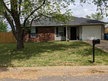 Single-story brick house with a large tree and mailbox in front yard.