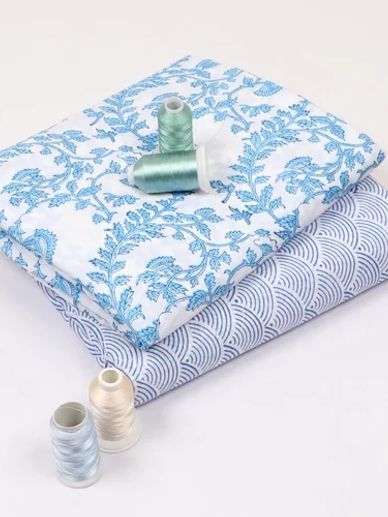 Two patterned fabrics with sewing threads on a white background.