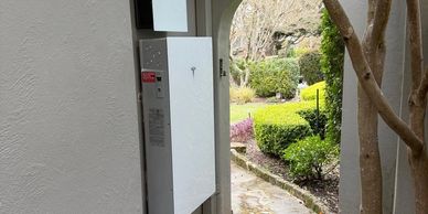 Outdoor electric panel on a white wall near garden path.
