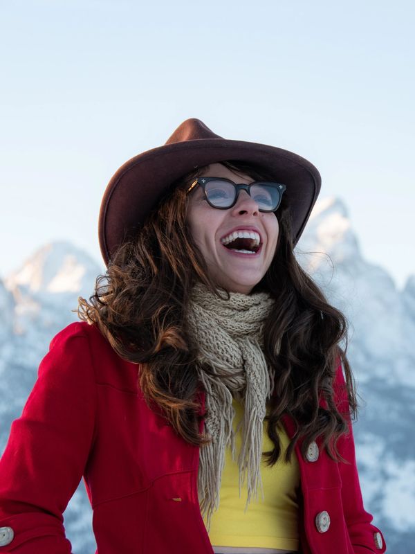 Anne Marie Wells laughing with mountain silhouettes behind her. She is wearing an unbuttoned red coa