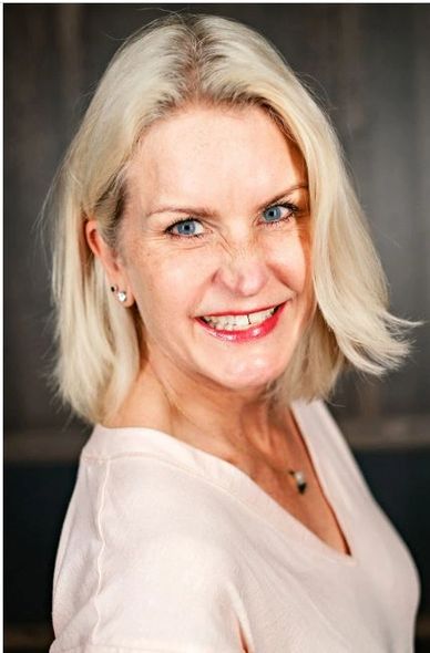 Smiling blonde woman with blue eyes in light top.