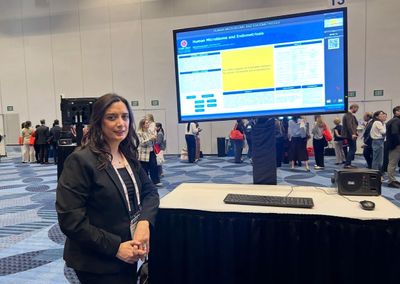 Woman presenting research poster at a conference with attendees in the background.