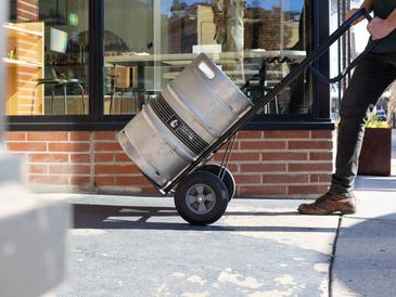 Person transporting a beer keg on a hand truck.