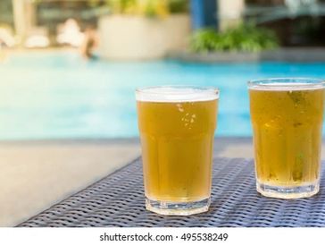 Two glasses of beer near a pool.