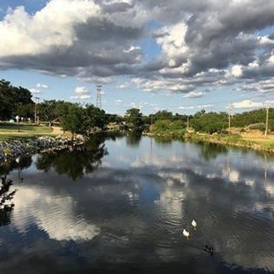 Calm river reflecting cloudy sky with ducks swimming.
