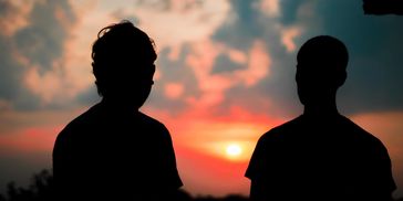 Two people silhouetted against a vibrant sunset sky.