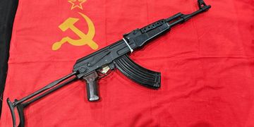 An AK-47 rifle placed on a red Soviet flag with hammer and sickle symbol.