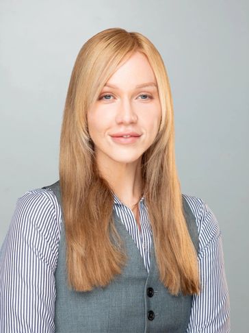 Confident woman with long blonde hair wearing a striped shirt and gray vest.