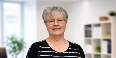 Smiling elderly woman with glasses in a bright modern office.