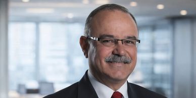 Portrait of a smiling middle-aged man in a suit and glasses in an office setting.
