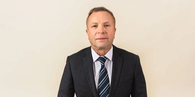 Professional man in a black suit and striped tie against a beige background.