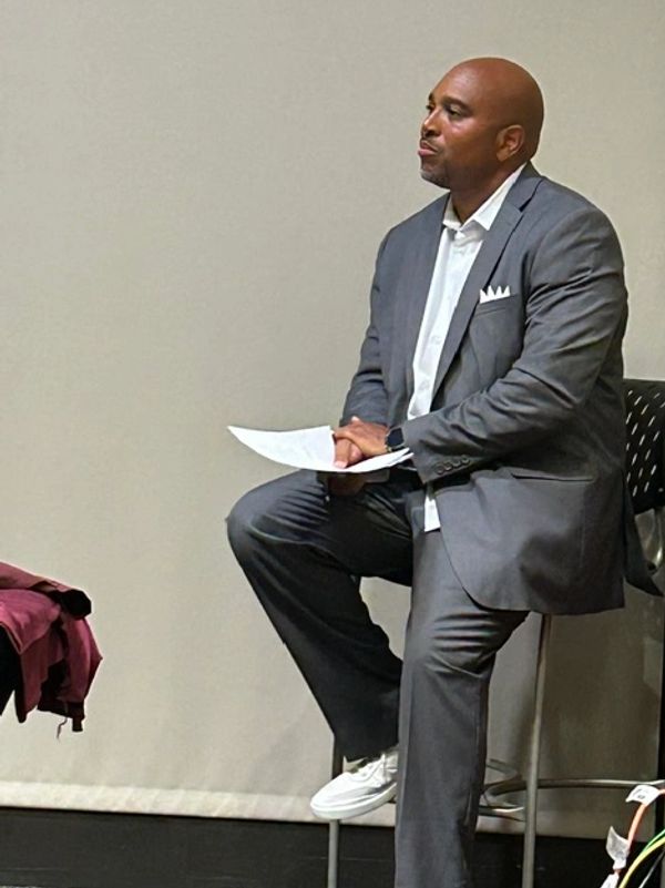 Man in gray suit sitting thoughtfully holding papers.