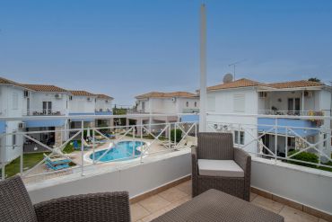 View from a balcony overlooking a swimming pool and white houses with terracotta roofs.