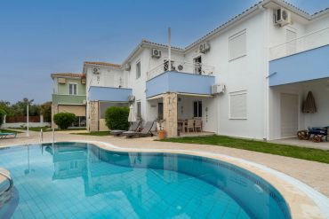 Modern white and blue houses with a swimming pool in front under a clear sky.