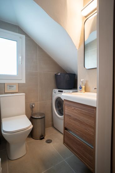 Compact bathroom with toilet, washing machine, and wooden vanity under sloped ceiling.