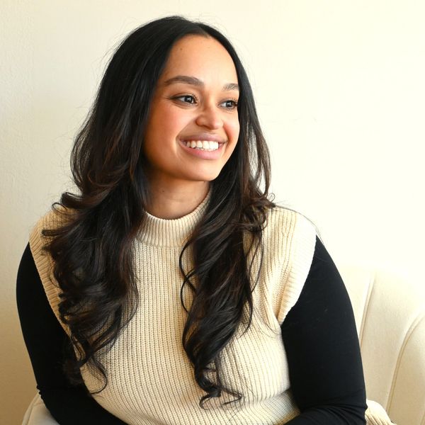 A smiling woman with long dark hair wearing a cream sweater vest and black top.