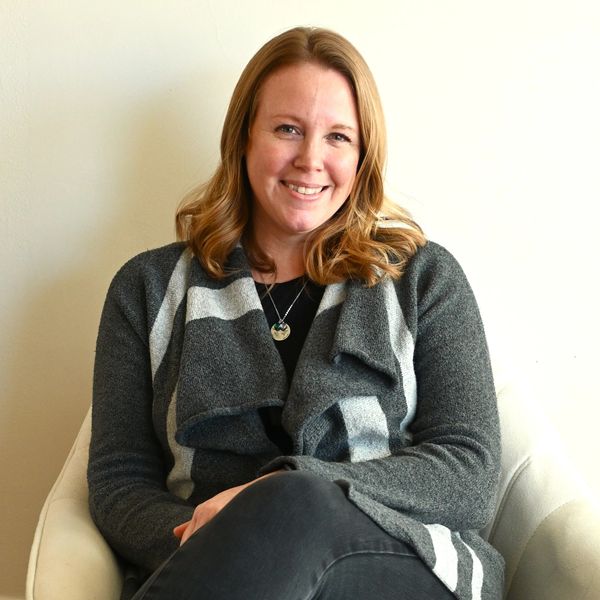 Smiling woman with light brown hair sitting comfortably in a chair.
