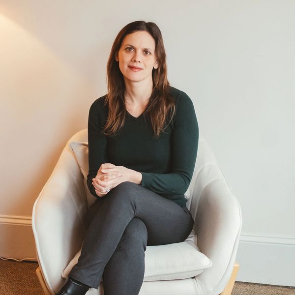 Woman sitting comfortably in a white armchair, smiling gently.