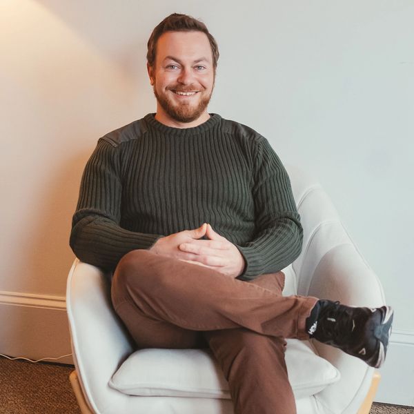 Man sitting comfortably in a white chair, smiling warmly at the camera.
