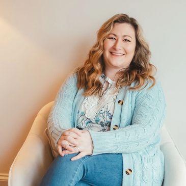 Smiling woman in a cozy blue cardigan sitting in a white chair.