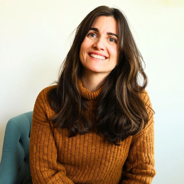 Smiling woman with long brown hair wearing a cozy mustard sweater.