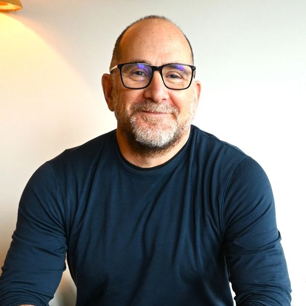 Middle-aged man smiling warmly wearing glasses and a dark shirt.