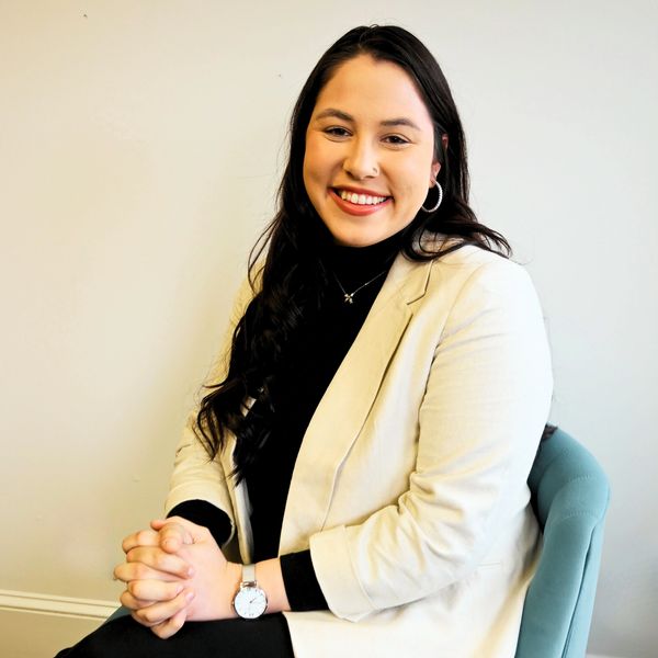 Smiling woman in a beige blazer sitting on a blue chair.