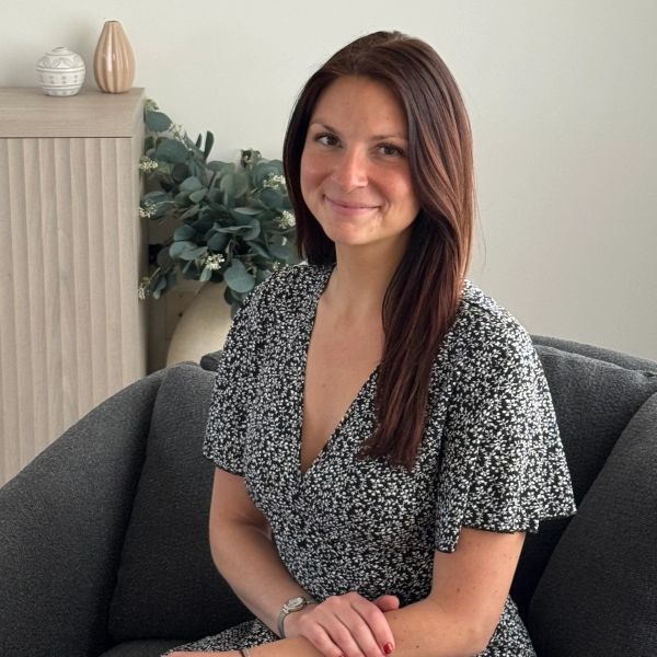 Woman sitting on a gray couch, smiling gently.