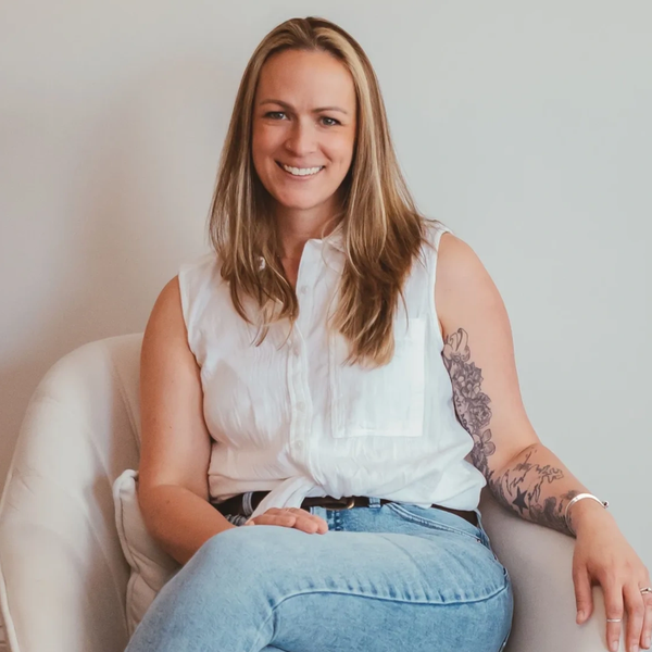 Smiling woman with tattoos, sitting comfortably on a white chair.