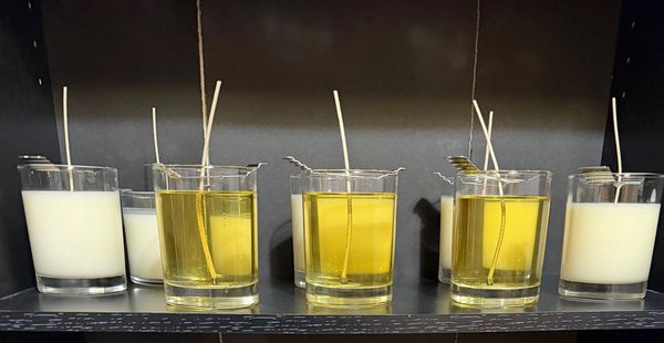 Rows of candles in glass containers, some with yellow wax and others with white wax.