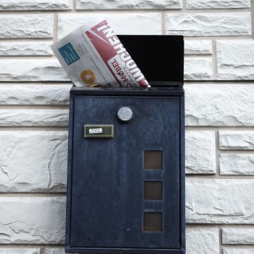 Mail delivered in a black mailbox against a white brick wall.